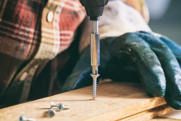 Person schraubt Holzbrett mit Akkuschrauber fest.